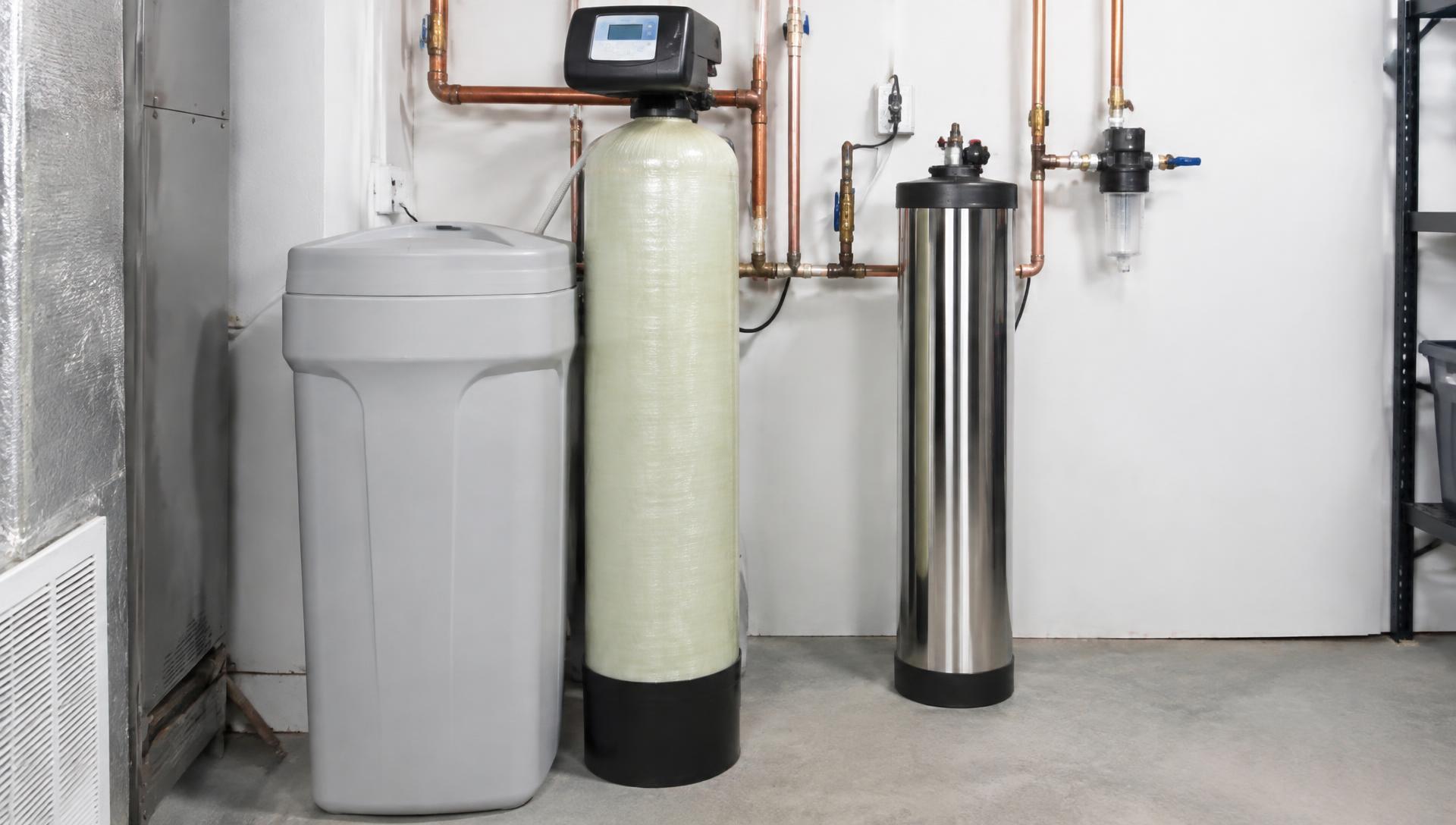 A salt-based water softener with a brine tank beside a compact salt-free conditioner in a bright utility room